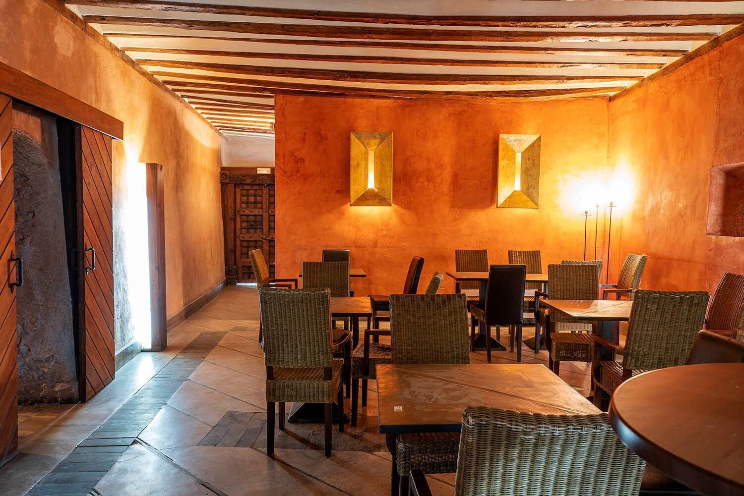 A restaurant with a rustic interior, featuring wooden walls and ceiling, and a long dining area with wicker chairs and tables.