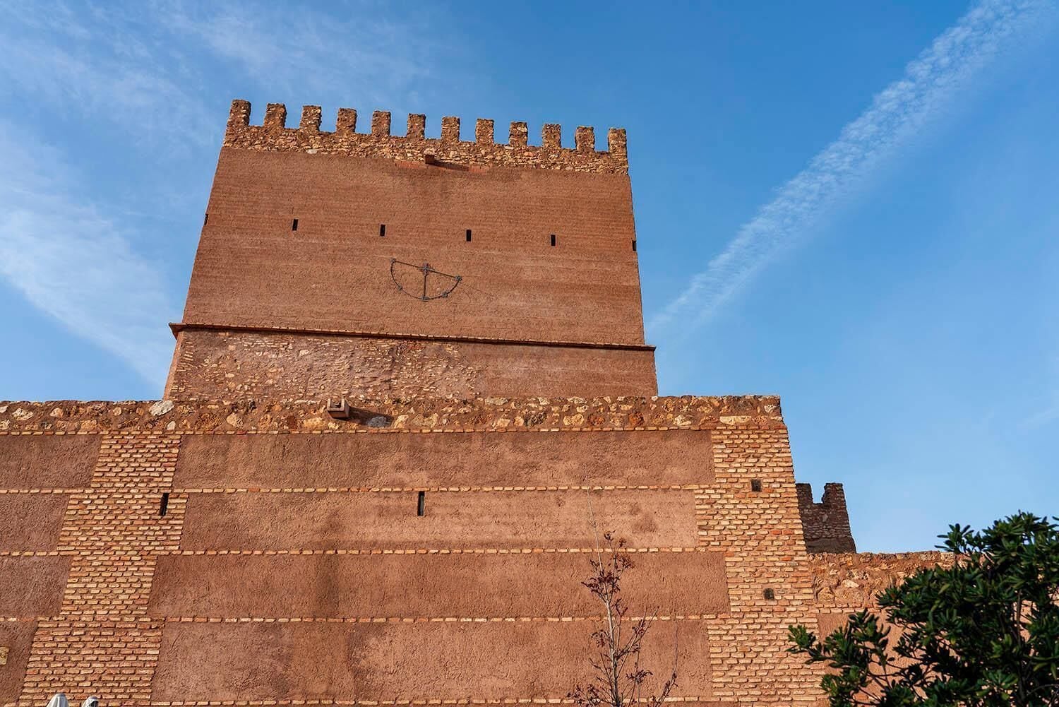 Una gran torre de ladrillo histórica con una parte superior almenada y una esfera horaria.