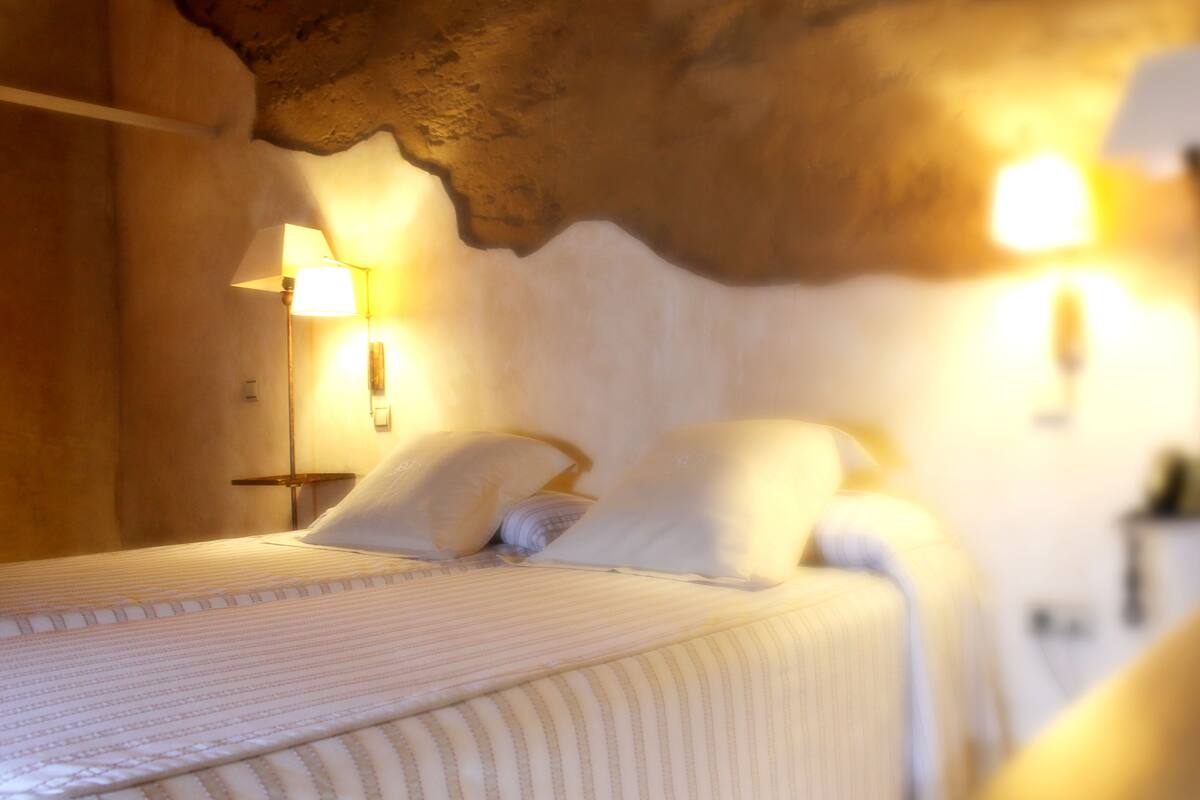 Een bed met witte lakens en kussens, een bedlampje en een muur met een structuur.