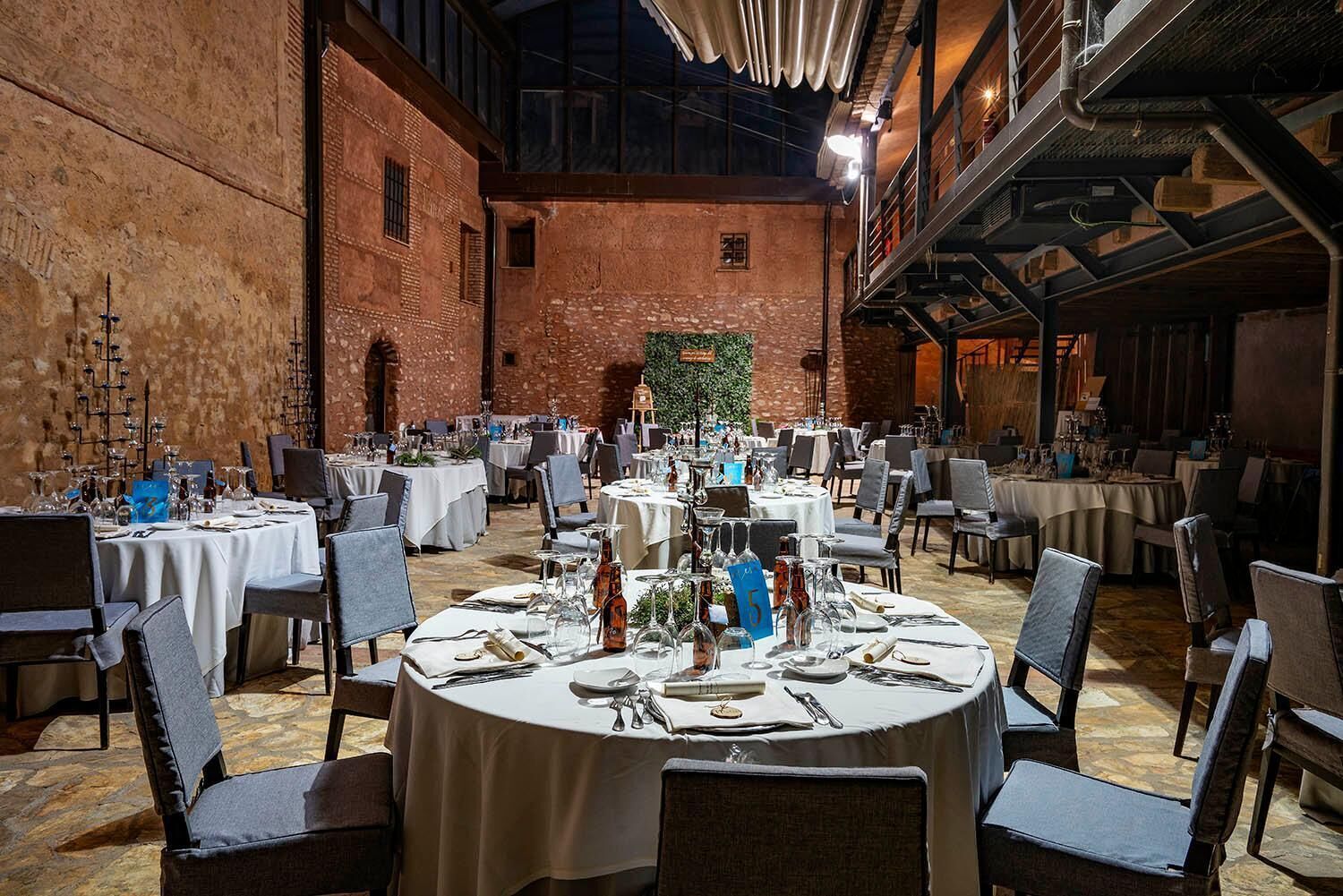 A spacious dining area with round tables, chairs, and a brick wall backdrop.
