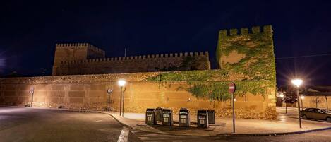 Un muro de piedra histórico con una estructura parecida a un castillo al fondo, un camino pavimentado y una hilera de buzones.