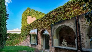 A building with ivy-covered walls, stone arches, and a statue in one of the windows. - Hotel Castillo de Pilas Bonas (Manzanares)