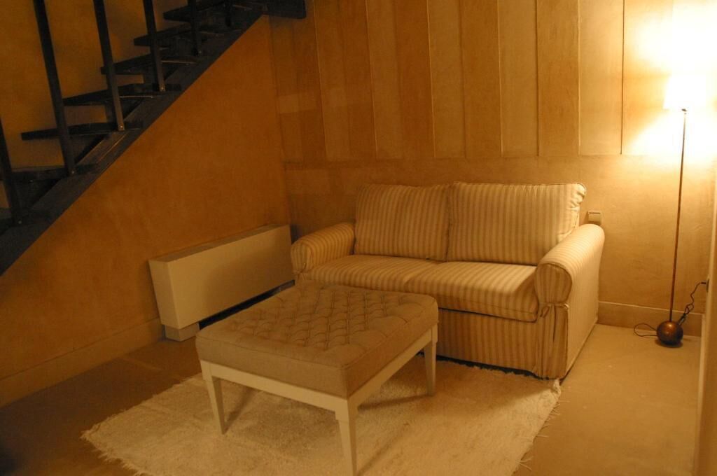 A room with a sofa, a small ottoman, a radiator, and a staircase.
