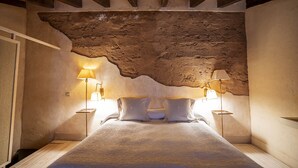 A bedroom with a rustic stone ceiling, a bed with white bedding, and two bedside lamps. - Hotel Castillo de Pilas Bonas (Manzanares)