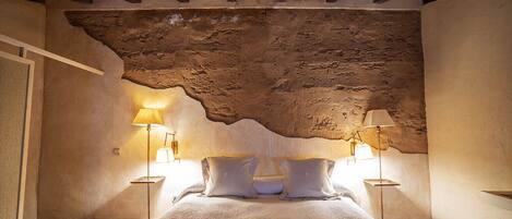 A bedroom with a rustic stone ceiling, a bed with white bedding, and two bedside lamps.