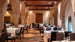 A restaurant with stone arches, wooden ceiling, and tables set for dining. - Hotel Castillo de Pilas Bonas (Manzanares)