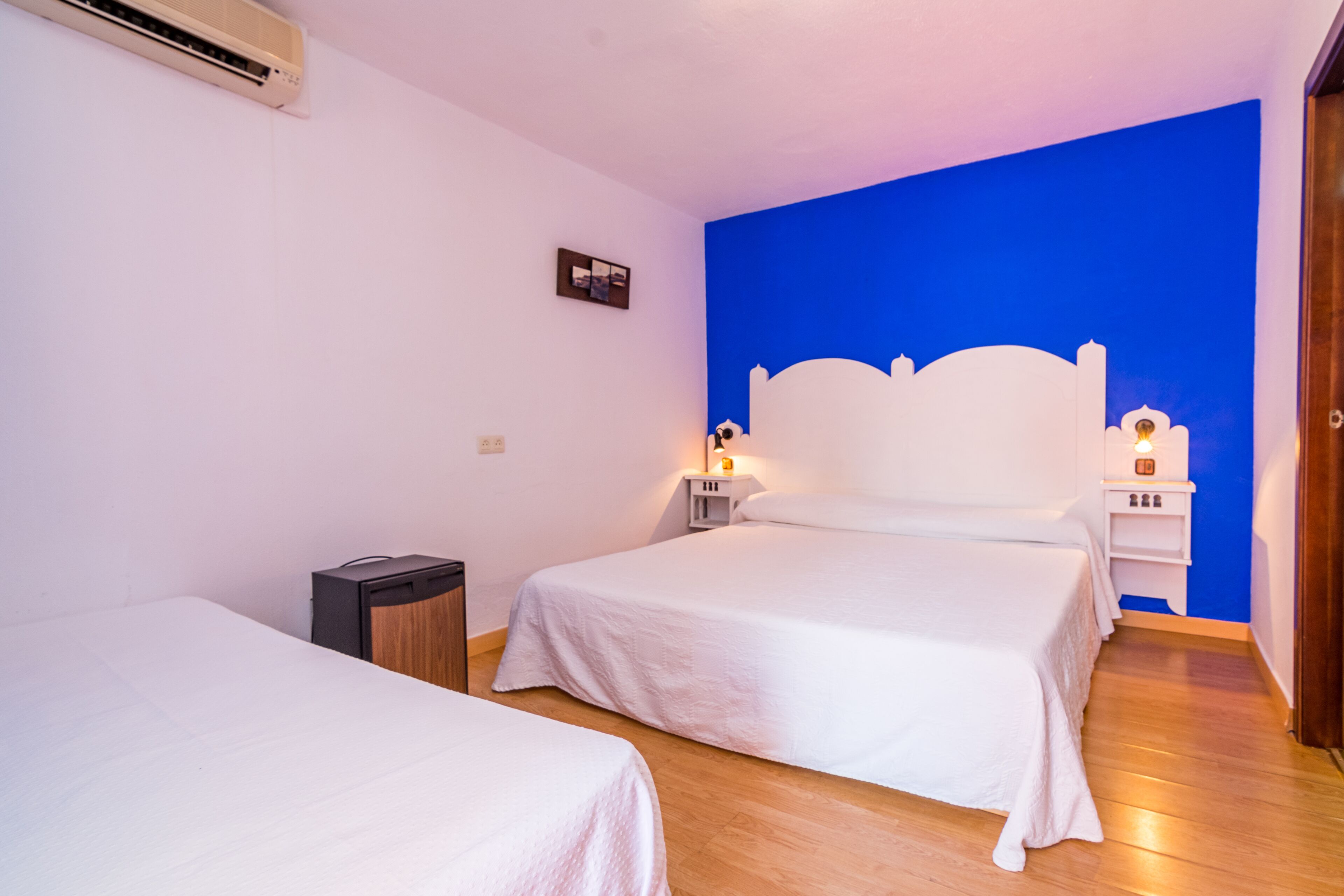 A hotel room with two single beds, a wooden floor, a white wall, and a blue accent wall.