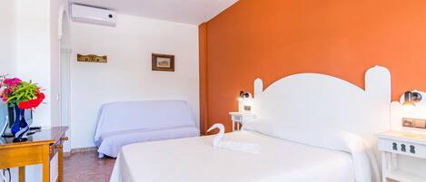 Un cuarto de hotel con una cama grande, una mesita de noche con una lámpara, un pequeño escritorio con un florero y un aire acondicionado instalado en la pared.