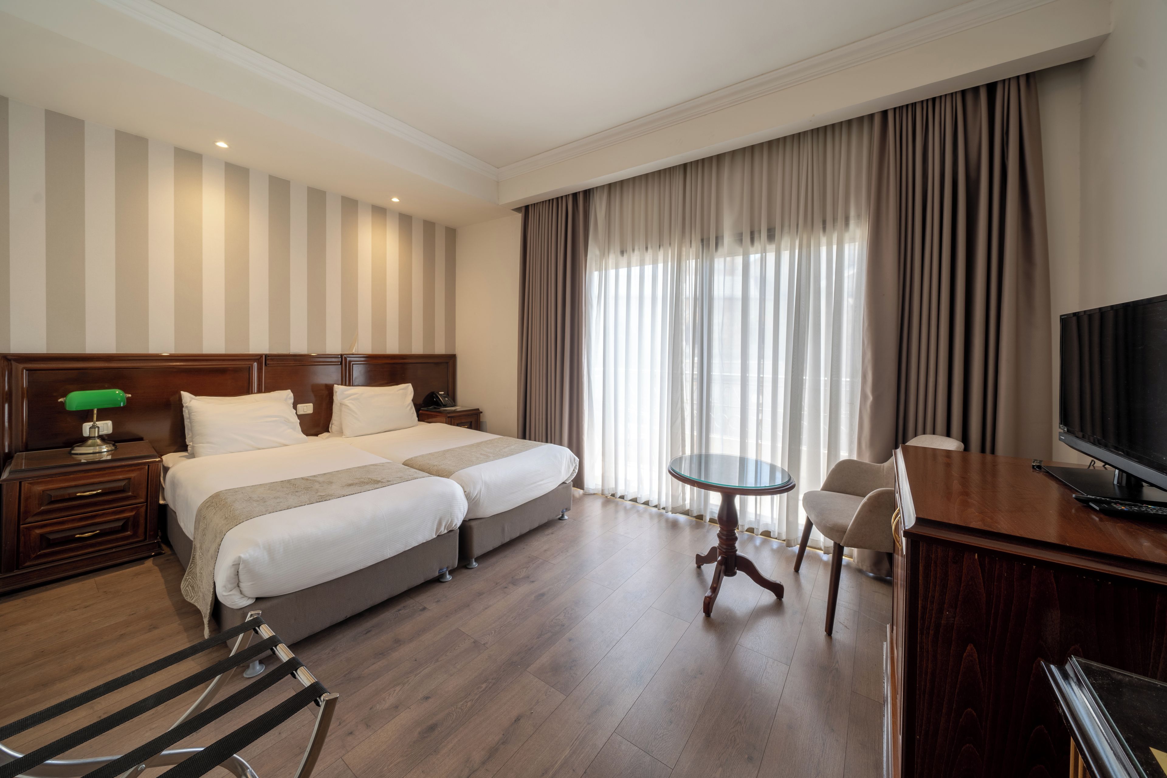 Habitación de hotel con cama doble, un escritorio con silla, televisión y un ventanal con cortinas.
