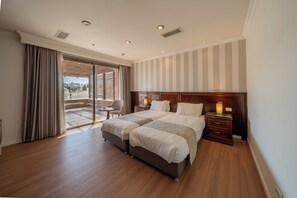A hotel room with two beds, a wooden floor, a large window with curtains, a view of the outside, and a nightstand with a lamp. - Christmas Hotel - Jerusalem (Jerusalem)