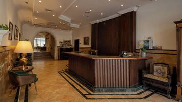 Een hotellobby met een receptiebalie, een zithoek en een trap naar een andere verdieping.