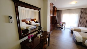 Habitación de hotel con un espejo grande, un escritorio con un florero, dos camas individuales, una mesita con sillas y una ventana con cortinas.
