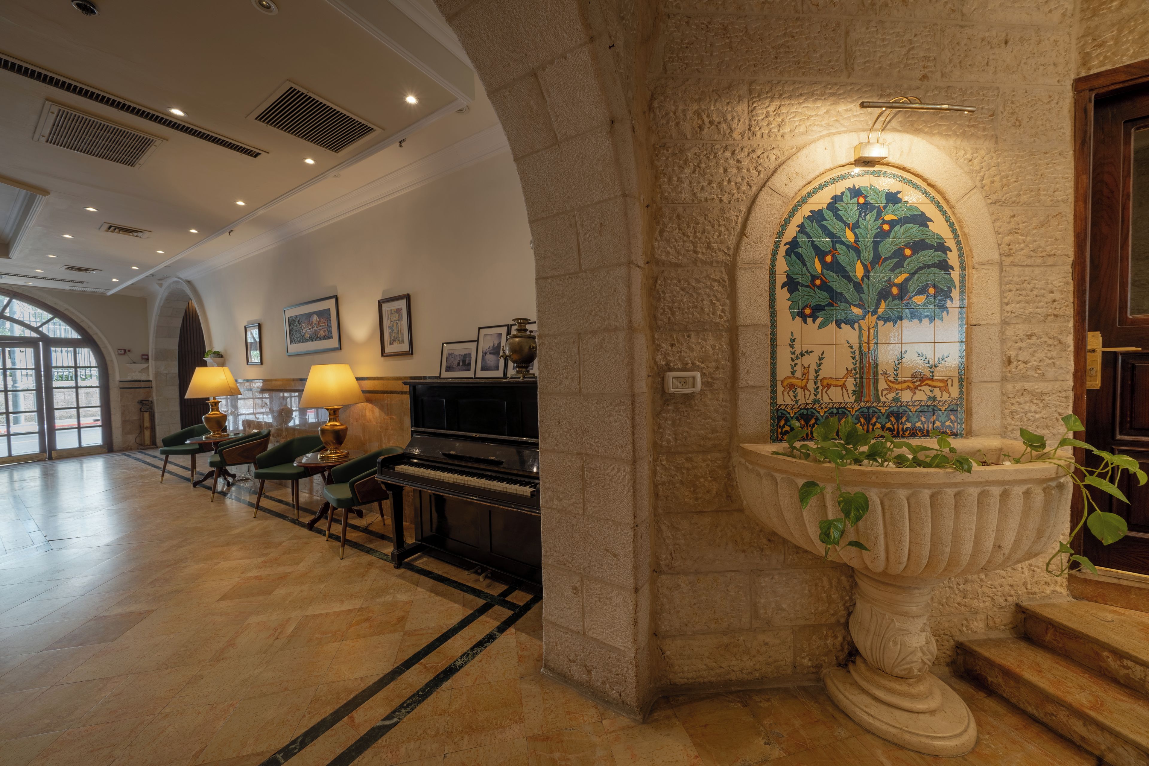 A lobby with a grand piano, a large decorative urn with plants, and a mural of a tree.