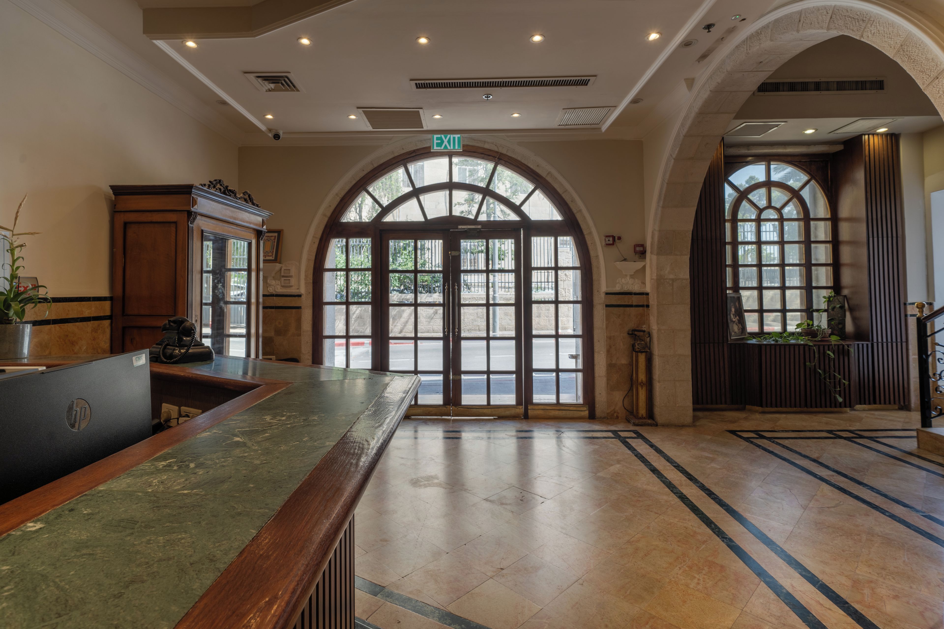 Un vestíbulo de hotel con una recepción, ventanas arqueadas y piso de baldosas.