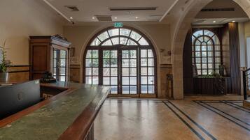 Un vestíbulo de hotel con una recepción, ventanas arqueadas y piso de baldosas.