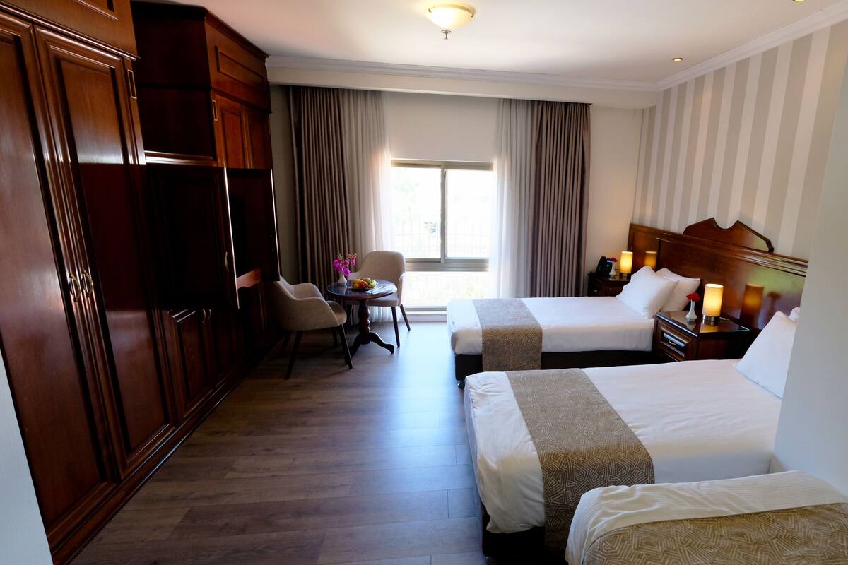 A hotel room with two beds, a desk, a chair, and a wardrobe.