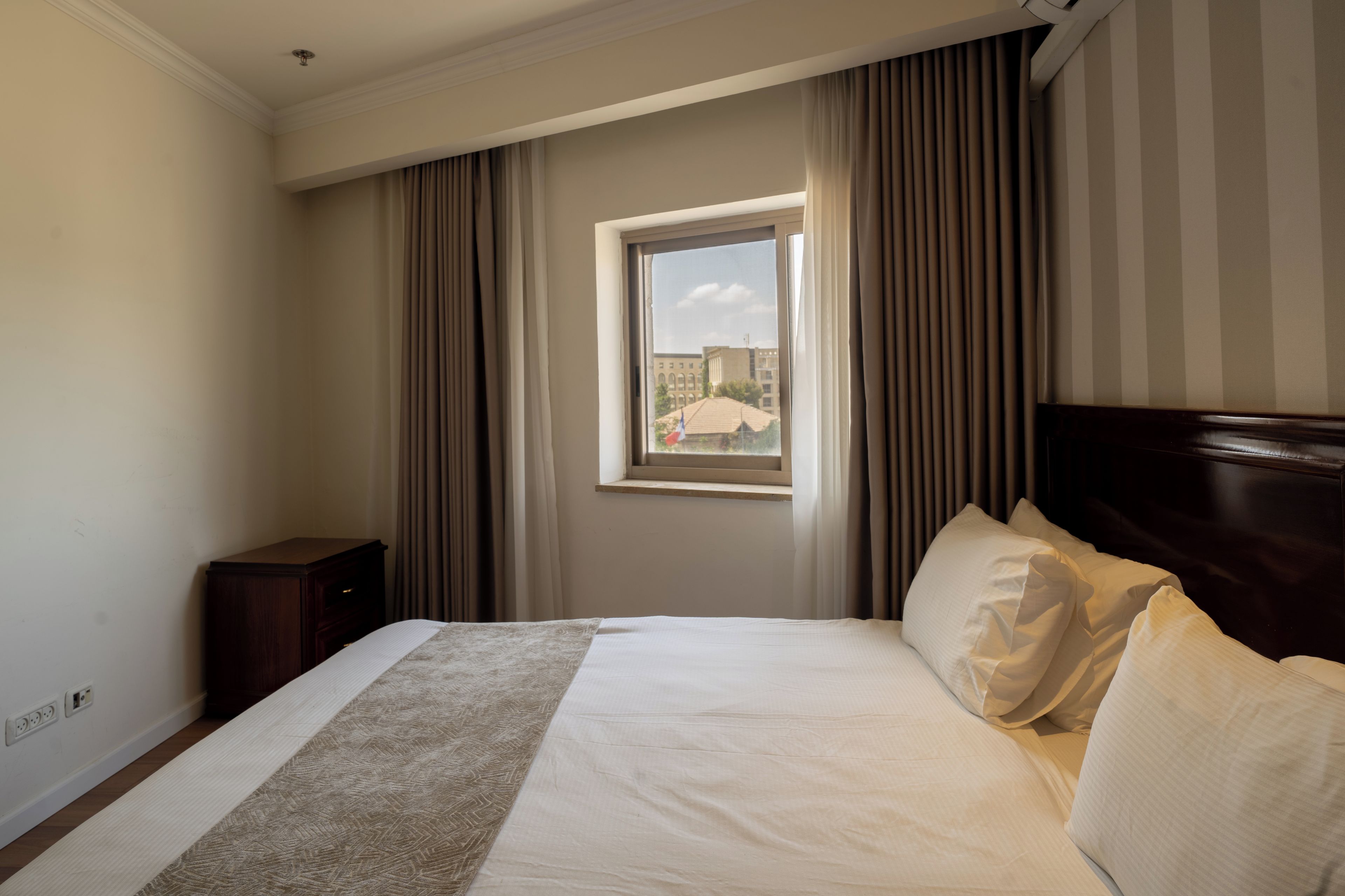 Una habitación de hotel con cama, ventana, cortinas y una mesita de noche.