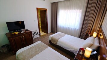 Habitación de hotel con dos camas, un televisor, un escritorio con frutero y la puerta del baño.