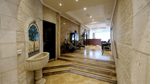 Un vestíbulo imponente con una escalera de mármol, un lavamanos decorativo y una zona de estar con sillas y un sofá.