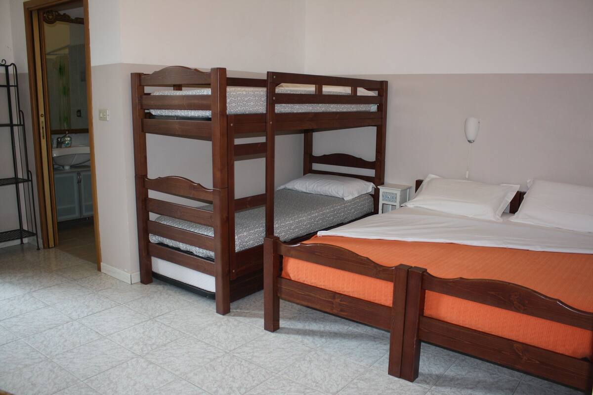 Una habitación con dos literas, una mesita de noche y un baño visible a través de una puerta abierta.