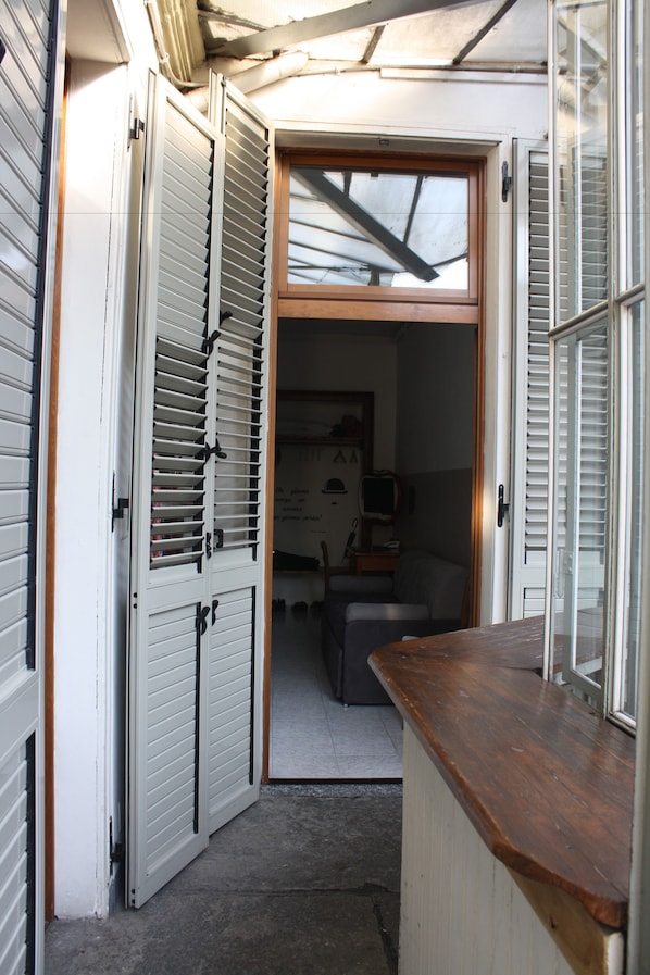 Un pasillo estrecho con un mostrador de madera y una puerta que da a una habitación con televisor y una silla.
