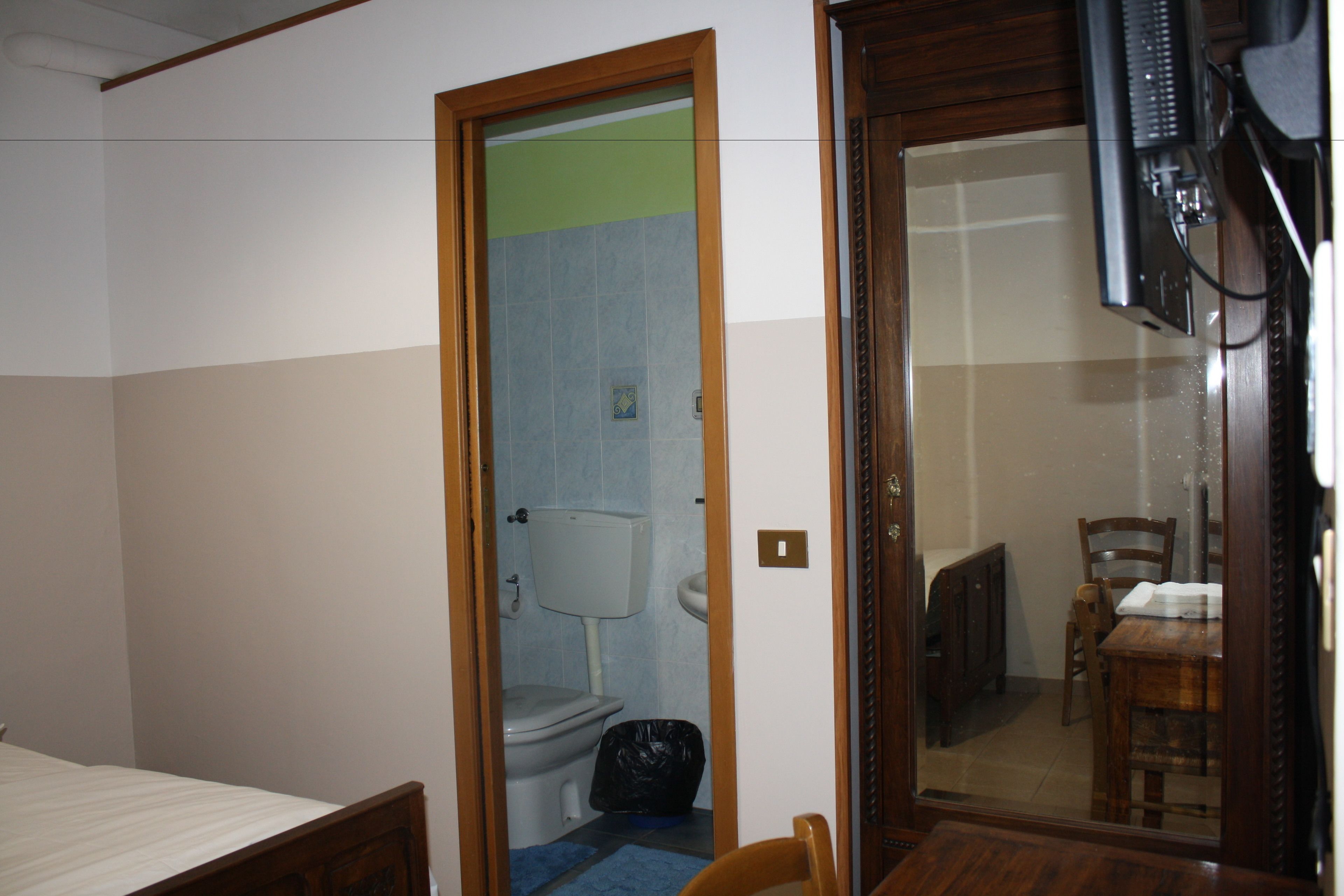 Ein Zimmer mit einem Bett, einem Holztisch, einem Stuhl, einem Badezimmer mit Toilette und einem Fernseher.