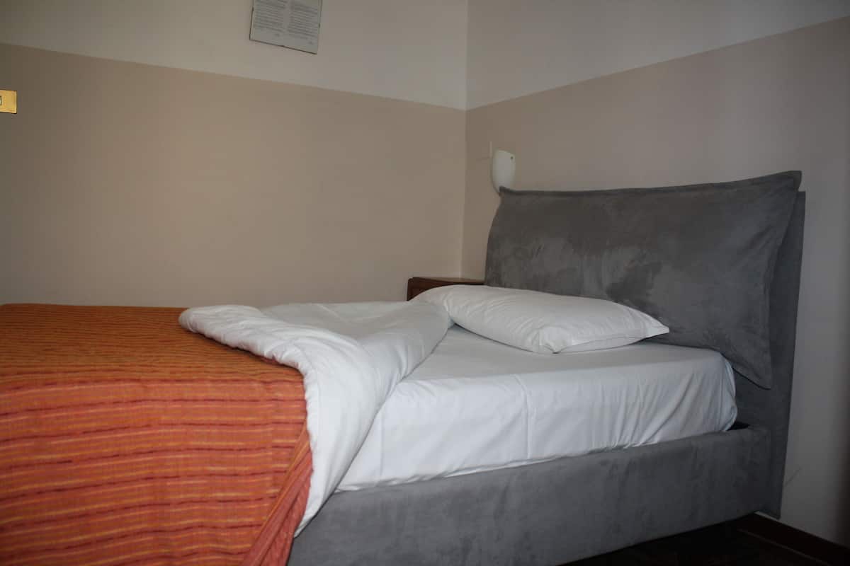Una cama bien hecha con cabecera gris y manta a rayas anaranjadas.
