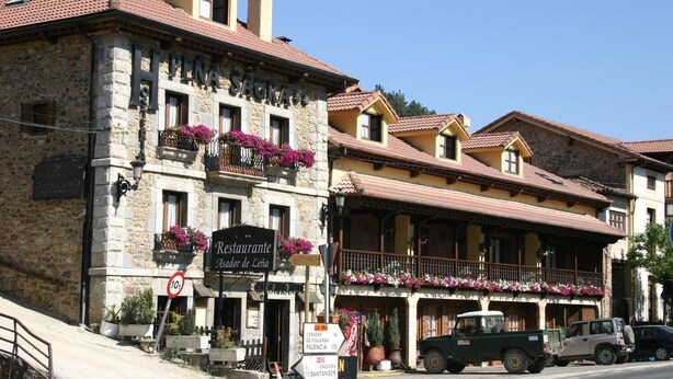 A stone building with a sign for Restaurante Asador de Leña, featuring balconies with flowers and a traditional architectural style. - Hosteria Peña Sagra (Cillorigo de Liebana)
