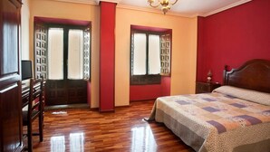 A bedroom with a wooden floor, a bed with a quilt, two windows with curtains, a wooden wardrobe, and a chandelier. - Hosteria Peña Sagra (Cillorigo de Liebana)