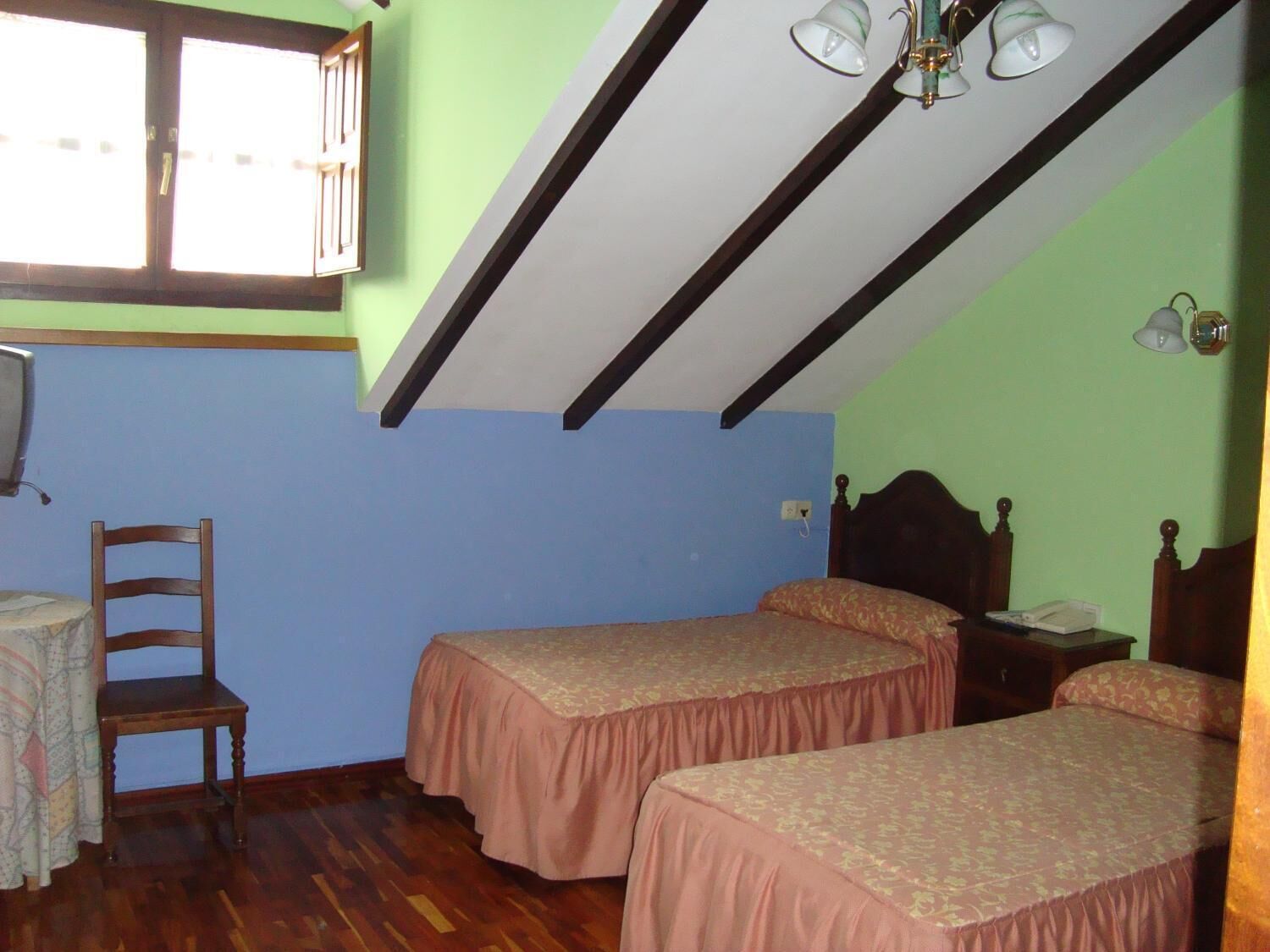 A room with two beds, a wooden chair, a small table, and a window with curtains.