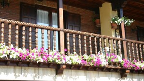 A balcony with wooden balusters and flower boxes containing pink and white flowers. - Hosteria Peña Sagra (Cillorigo de Liebana)