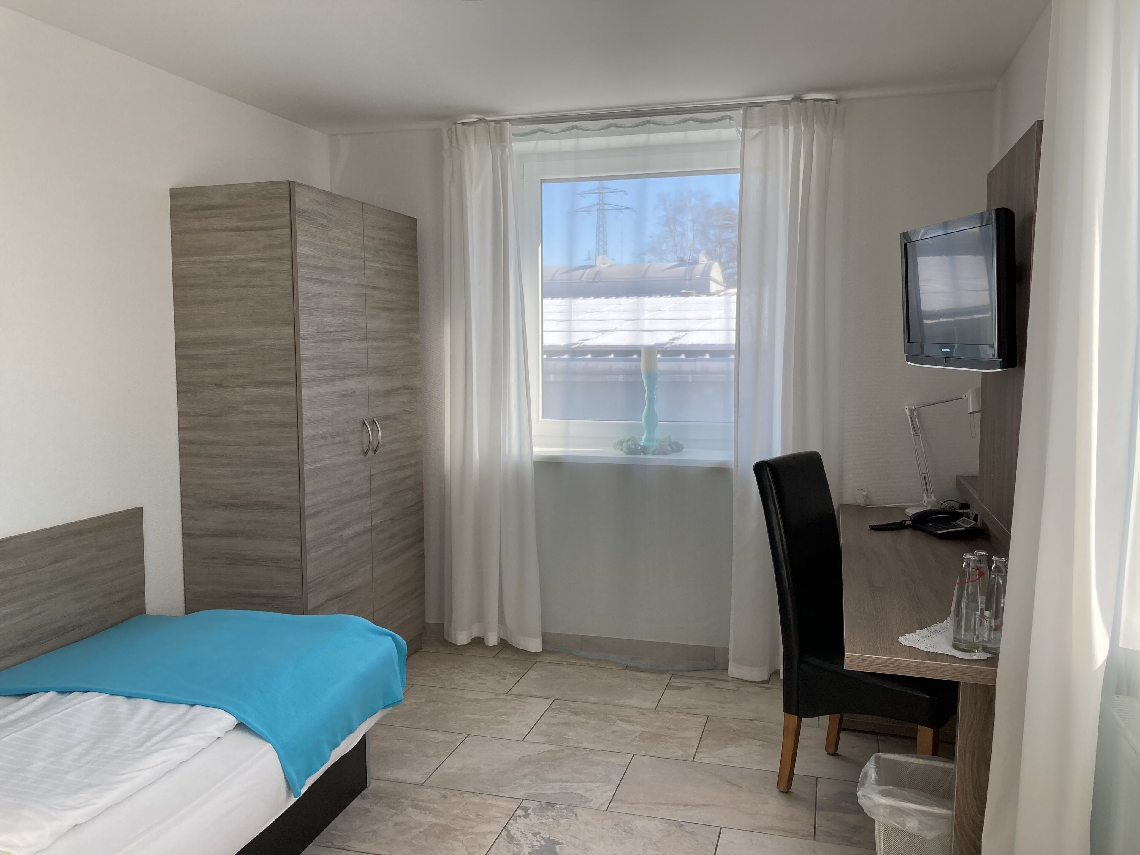 Ein Hotelzimmer mit Bett, Schreibtisch mit Stuhl, Fernseher und Kleiderschrank.