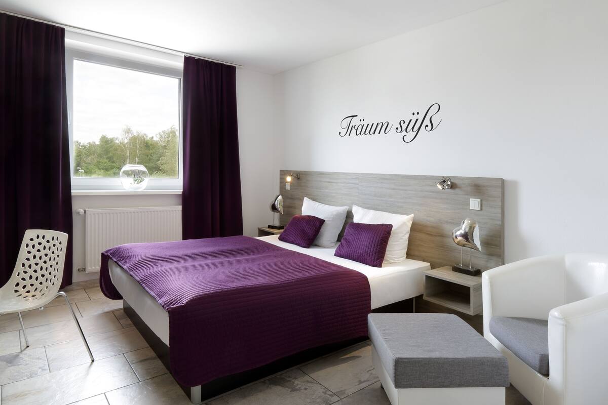 A modern bedroom with a large bed, a bedside table, a chair, and a view of the outdoors.