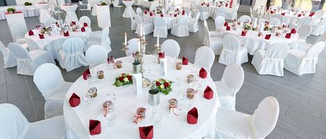 Un amplio salón de banquetes con mesas redondas dispuestas para un evento formal, con manteles blancos, servilletas rojas y centros de mesa florales.