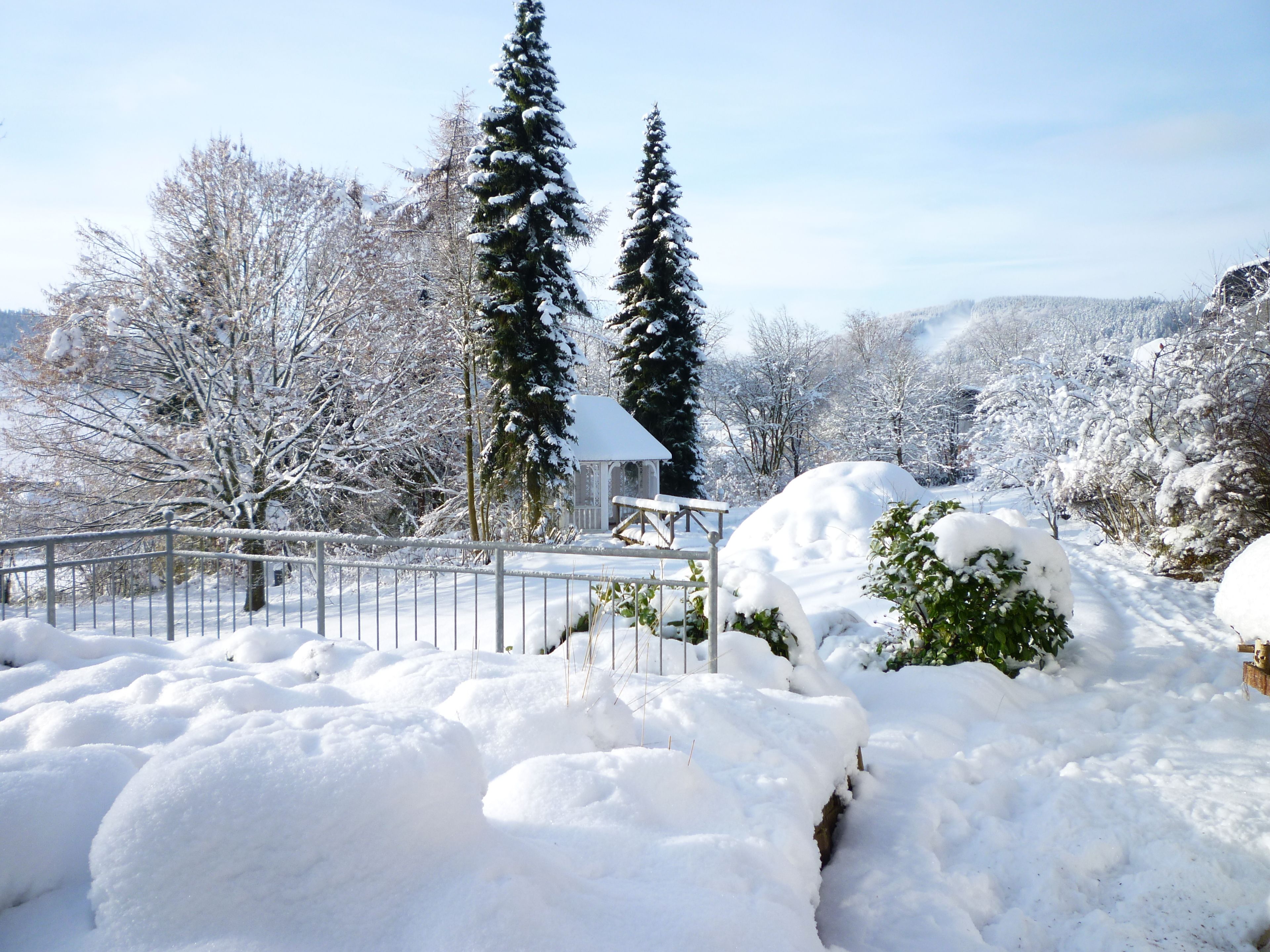 A snow-covered landscape with a wooden gazebo and a metal fence.