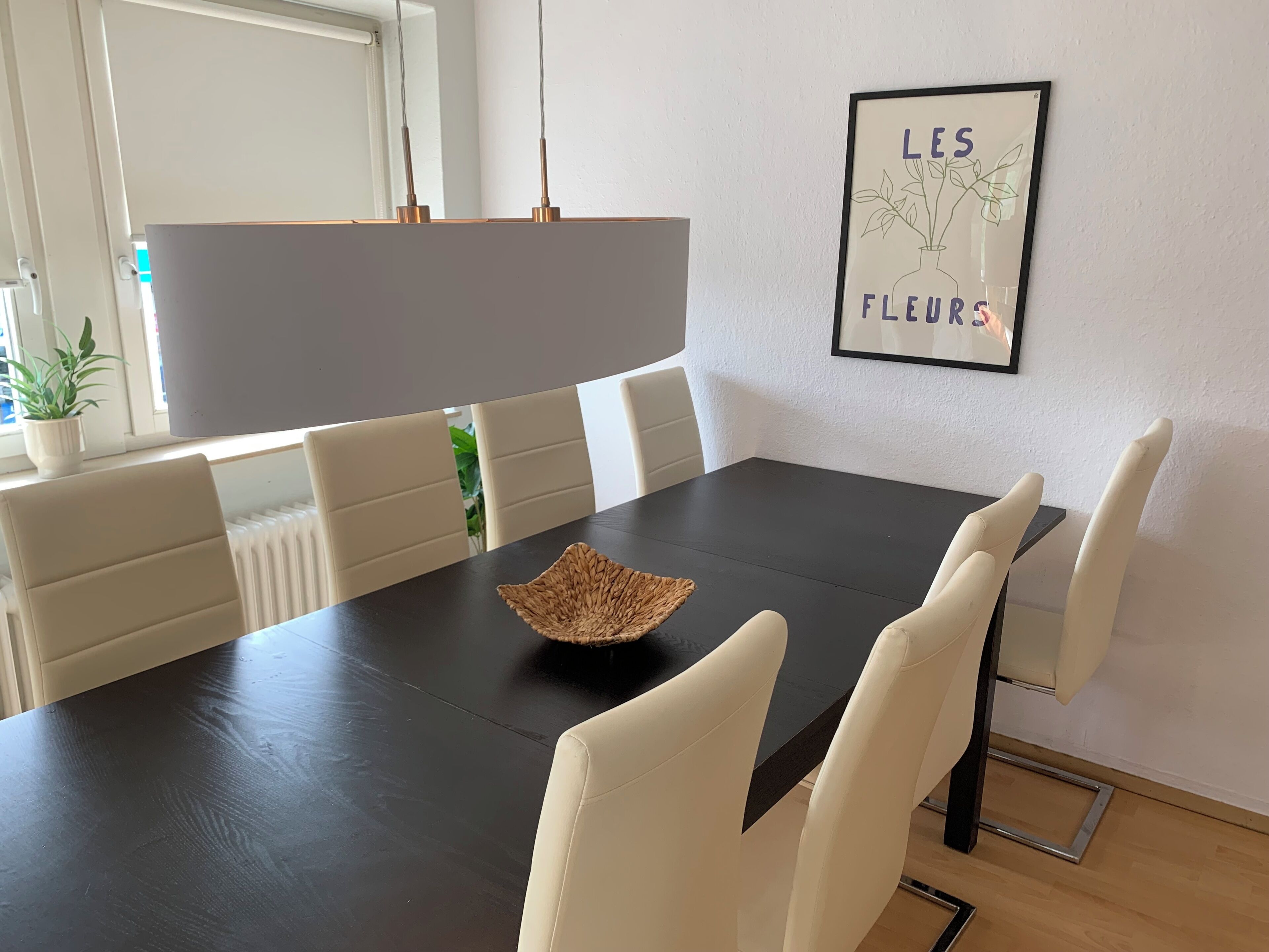 A dining area with a black table, white chairs, a woven bowl, and a framed picture on the wall.