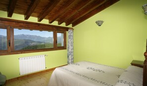 Un dormitorio con cama, radiador, ventana con vistas a montañas y techo de madera.