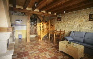 Un interior rústico con pared de piedra, escalera de madera, un sofá y una zona de cocina.