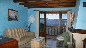 A cozy living room with a sofa, armchair, and a coffee table. A window offers a view of mountains.