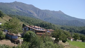 A traditional chalet-style building with multiple balconies, surrounded by lush greenery and mountains in the background.