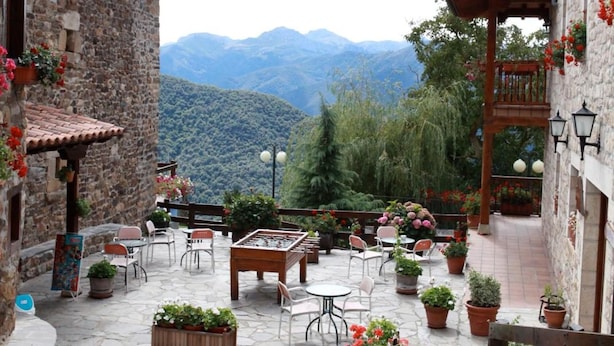 A courtyard with stone flooring, potted plants, outdoor seating, and a view of mountains.
