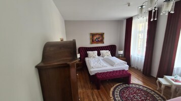 Un dormitorio con un escritorio de madera, una cama con cabecero rojo, una alfombra estampada y un cuadro en la pared.