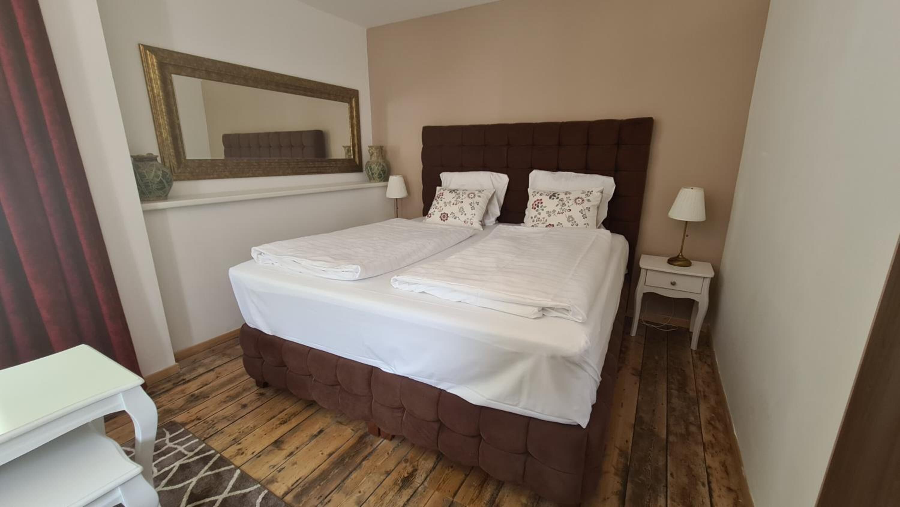 Una cama doble con ropa blanca de cama bien ordenada, un cabecero tapizado en marrón y dos lámparas de noche.