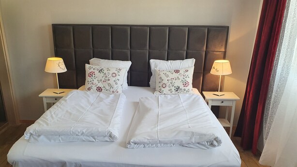 A neatly made bed with white linens, two decorative pillows with floral patterns, and two bedside lamps on matching nightstands. - Osteria Del Vino Cochem (Cochem)