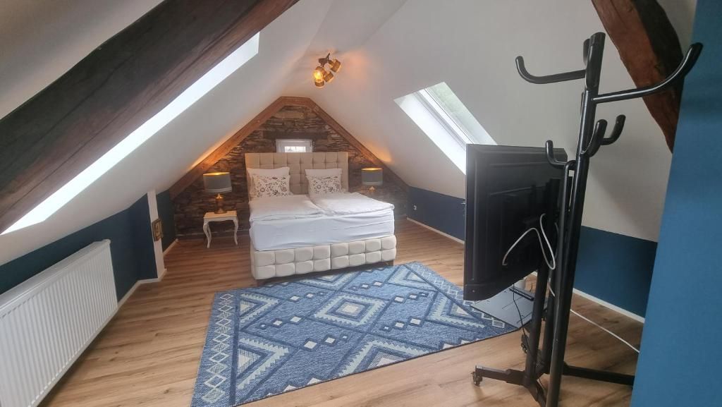 Un dormitorio con techo inclinado, una cama, un televisor y una pared de piedra.