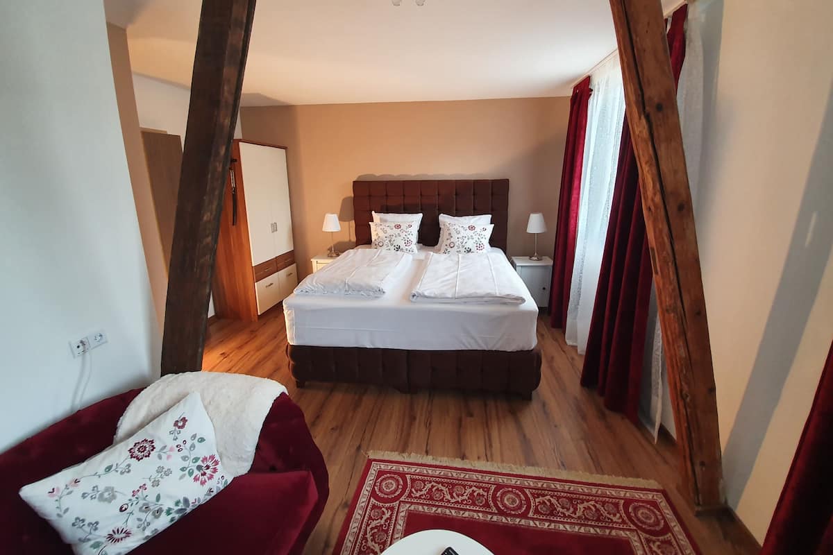 Um quarto com uma cama grande, vigas de madeira, um candelabro e um tapete com padrão vermelho e branco.