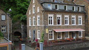 A two-story stone building with multiple windows, a red awning, and outdoor seating. - Osteria Del Vino Cochem (Cochem)