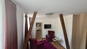 A room with a red armchair, a small round table, a television mounted on the wall, and a wooden beam structure. - Osteria Del Vino Cochem (Cochem)