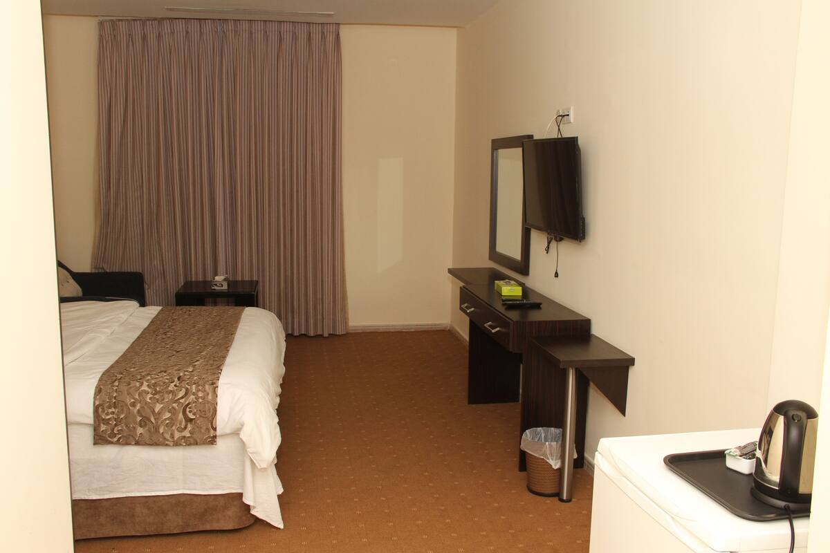 Quarto de hotel com cama, escrivaninha, cadeira, televisão e máquina de café.