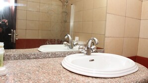A bathroom with a granite countertop, a white sink, and a mirror reflecting a shower area. - Jeddah Palace Hotel (Amman)